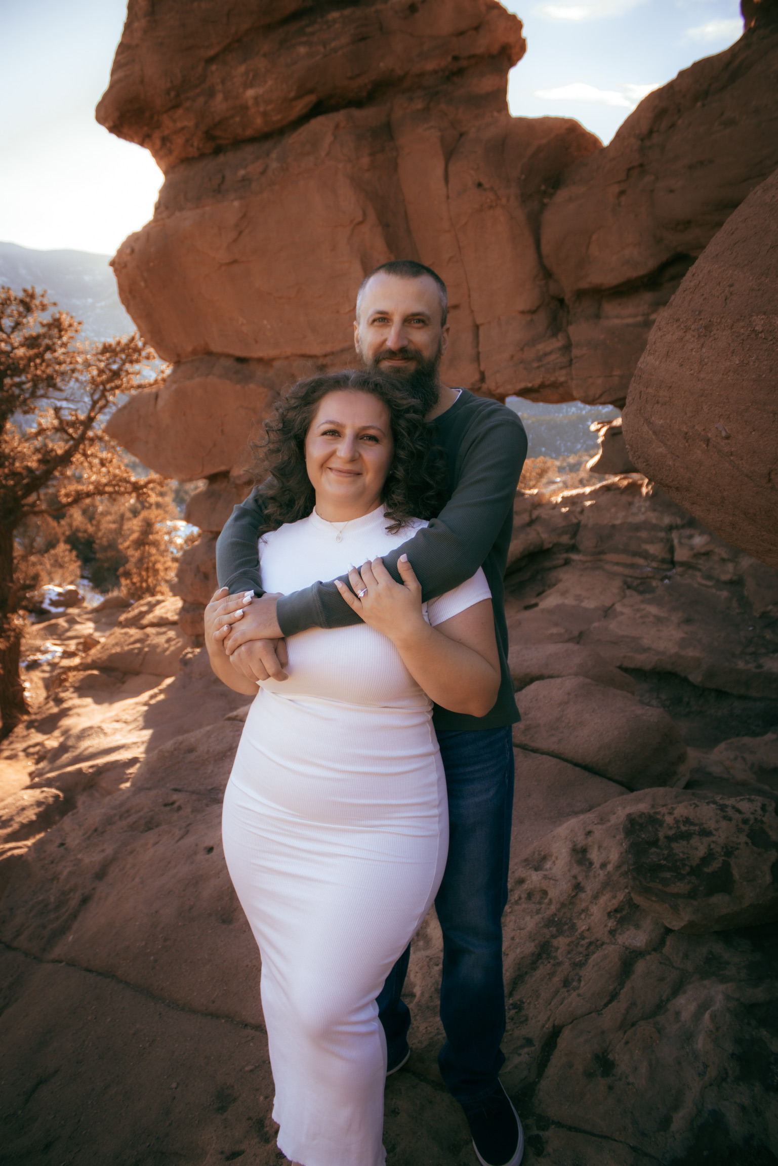 Adam and Emirjeta embracing under the red rock arch at Garden of the Gods